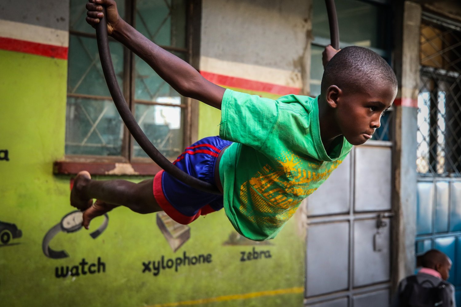 A boy in a bright green T-shirt swings from a gym ring at the One Fine Day Arts Centre in Nairobi.
