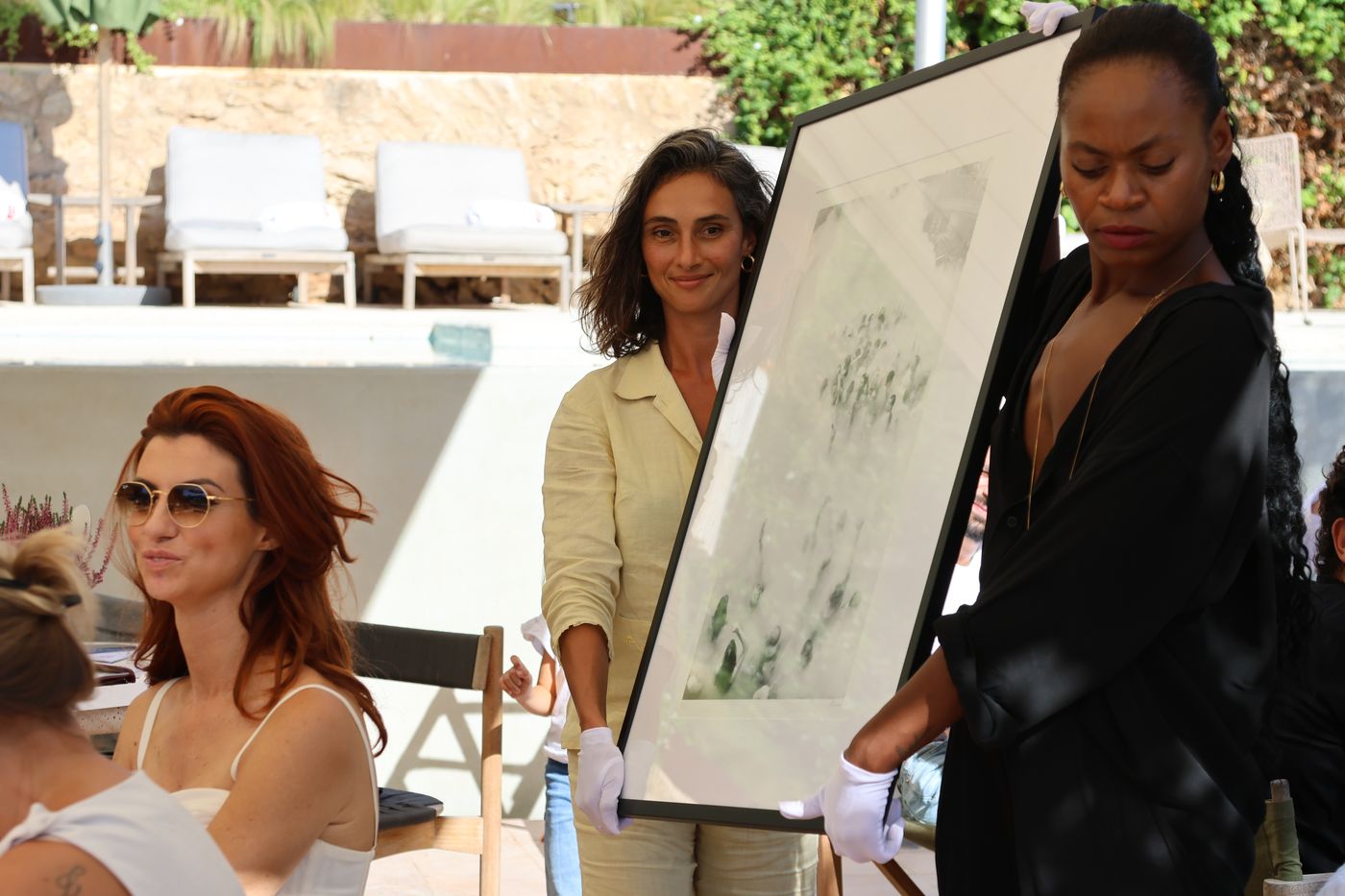 Two presenters in white gloves hold up a framed work for the guests.