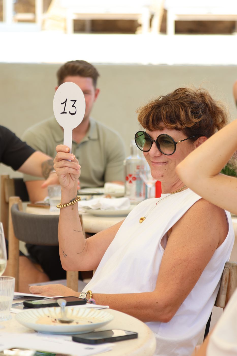 A guest in round sunglasses raises paddle 13.